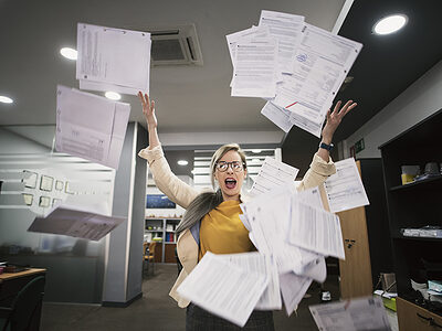 Stressed woman throws papers in the office in an image of relief Schlagwort(e): businessperson