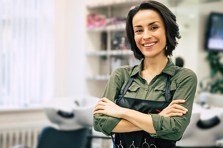 Portrait of a gorgeous young hairstylist standing with folded arms near her workplace in the salon.