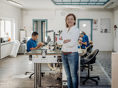 Zahntechnikermeisterin steht in ihrem Labor, im Hintergrund arbeiten Zahntechniker.