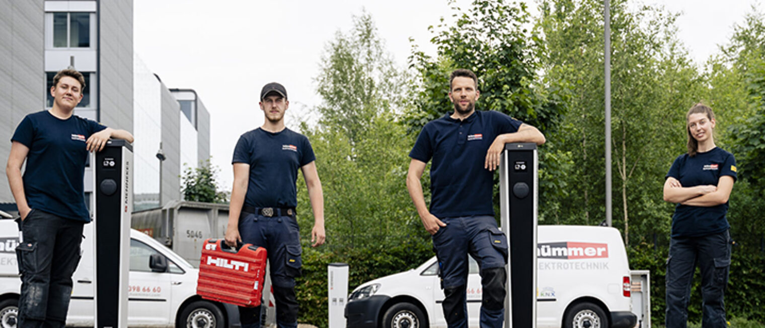 Mitarbeiter von Hümmer Elektrotecnhik und ad fontes Solartechnik stehen an Ladesäulen, Im Hintergrund: Nutzfahrzeuge.