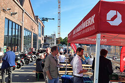 Grill unter Zeltdach, drei Personen stehen mit Tellern an