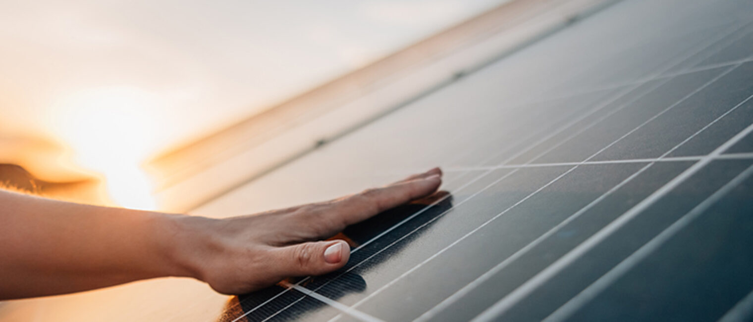 Hand berührt Solarkollektoren, im Hintergrund: Sonnenaufgang Hand berührt Solarkollektoren, im Hintergrund: Sonnenaufgang