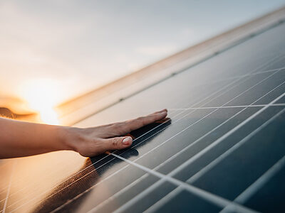 Hand berührt Solarkollektoren, im Hintergrund: Sonnenaufgang