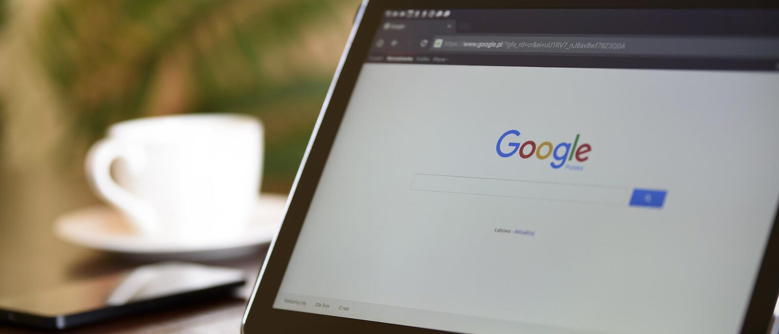 Google-Startseite auf einem Tablet. Im Hintergrund ein Smartphone und eine Kaffeetasse. Google-Startseite auf einem Tablet. Im Hintergrund ein Smartphone und eine Kaffeetasse.