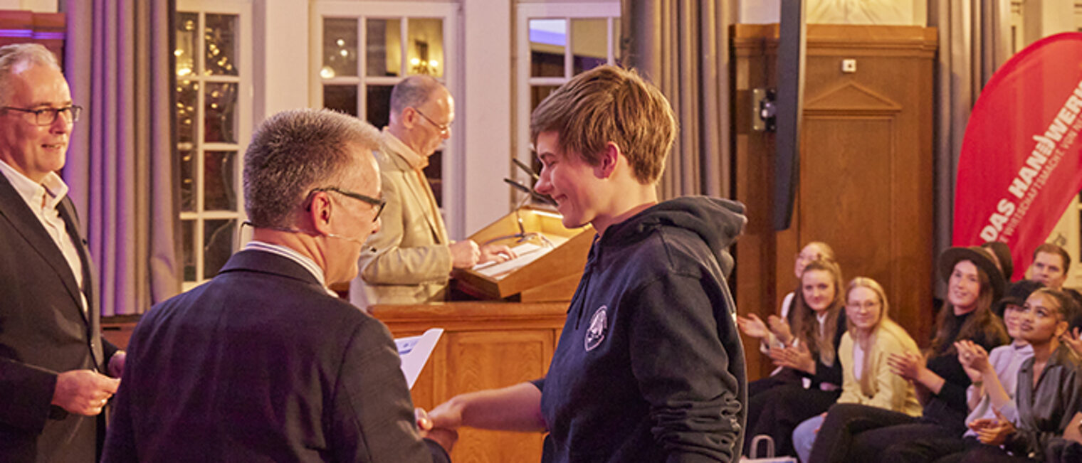 Präsident Hjalmar Stemmann gratuliert der Landessiegerin im Bootsbauer-Handwerk auf der Bühne. Präsident Hjalmar Stemmann gratuliert der Landessiegerin im Bootsbauer-Handwerk auf der Bühne.