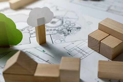 Bauzeichnung, darauf Bauklötze aus Holz und aus Papier gebastelte Bäume