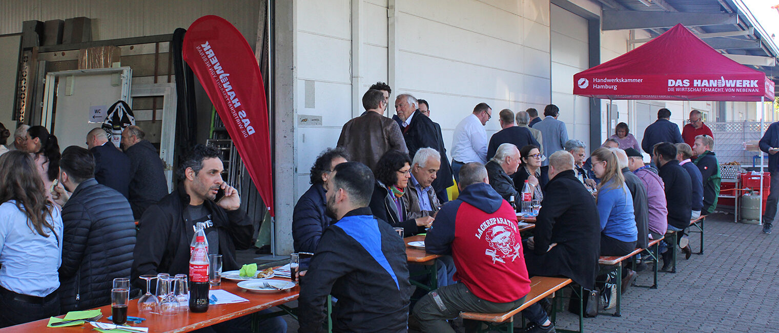 Handwerker*innen im Gespräch auf Bierbänken vor einer Werkhalle Handwerker*innen im Gespräch auf Bierbänken vor einer Werkhalle