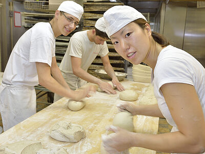 Zwei junge Bäcker und eine Bäckerin formen Teig zu Broten.