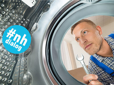 Handwerker blickt in eine Waschmaschine, um sie zu reparieren.