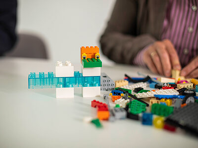 Erwachsener baut auf einem Tisch etwas mit Legosteinen.