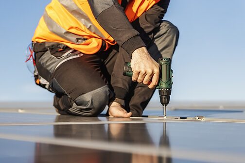 Handwerker befestigt Solarpanels auf einem Dach mit einer Bohrmaschine