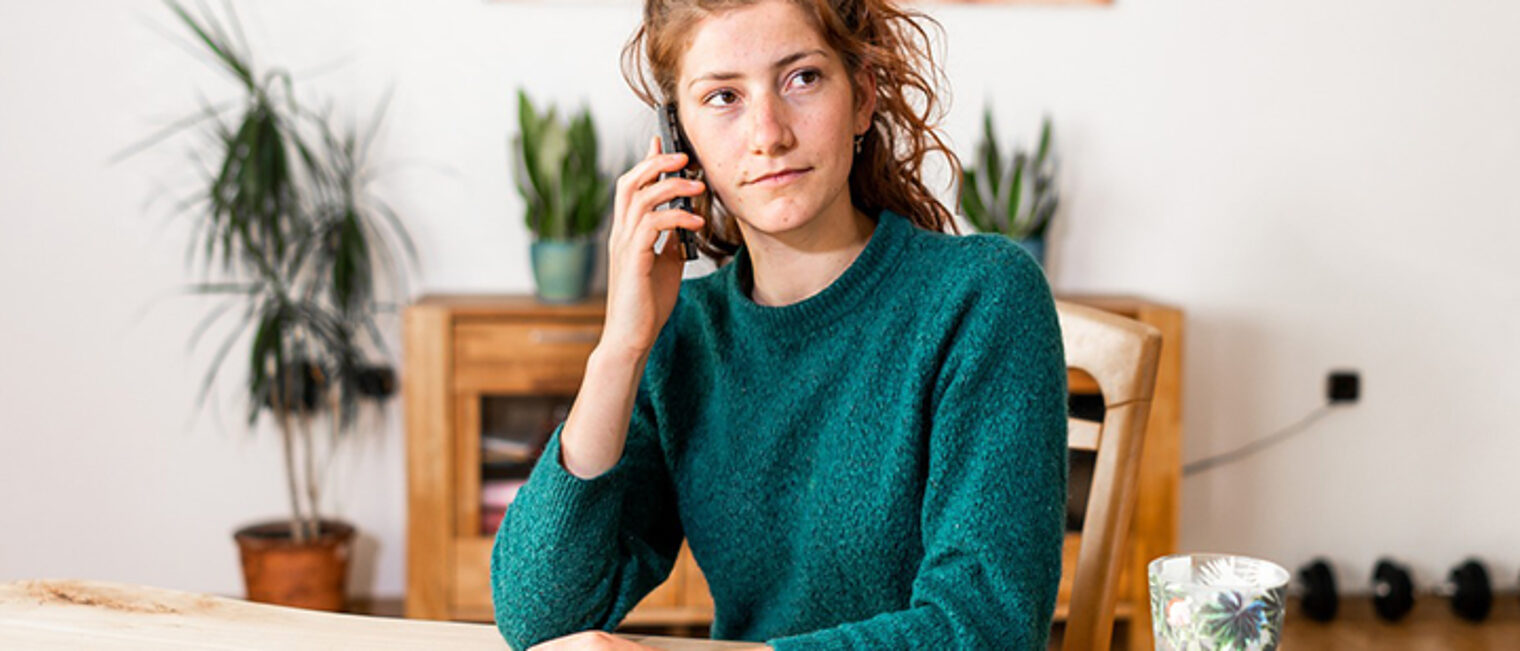 Junge Frau sitzt am Tisch und telefoniert.