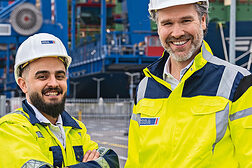 zwei bärtige Männer im Hafen mit Arbeitskleidung und Helm
