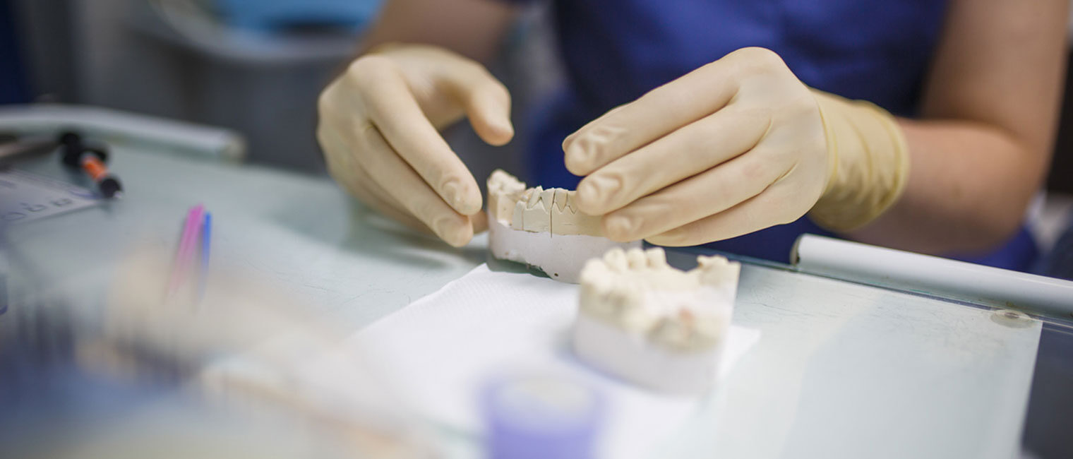 Hände mit Handschuhen bearbeiten ein Modellgebiss