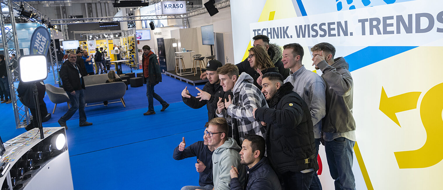 Gruppe Jugendlicher vor Fotowand auf einer Messe.
