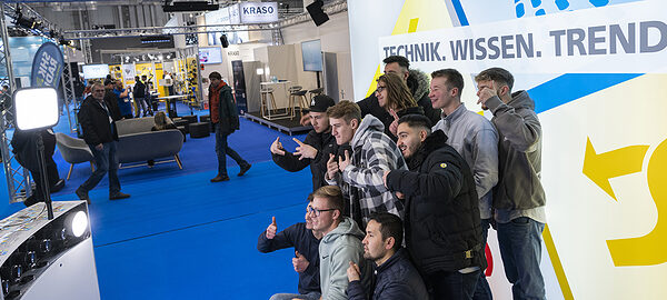 Gruppe Jugendlicher vor Fotowand auf einer Messe.