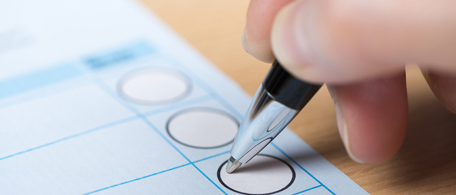 Hand führt Kugelschreiber auf Wahlzettel.