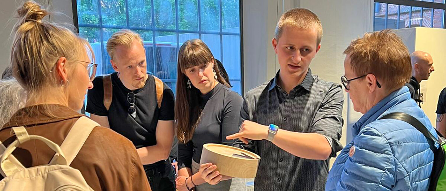 Junger Tischler erläutert Interessierten sein Werkstück, eine Schale.