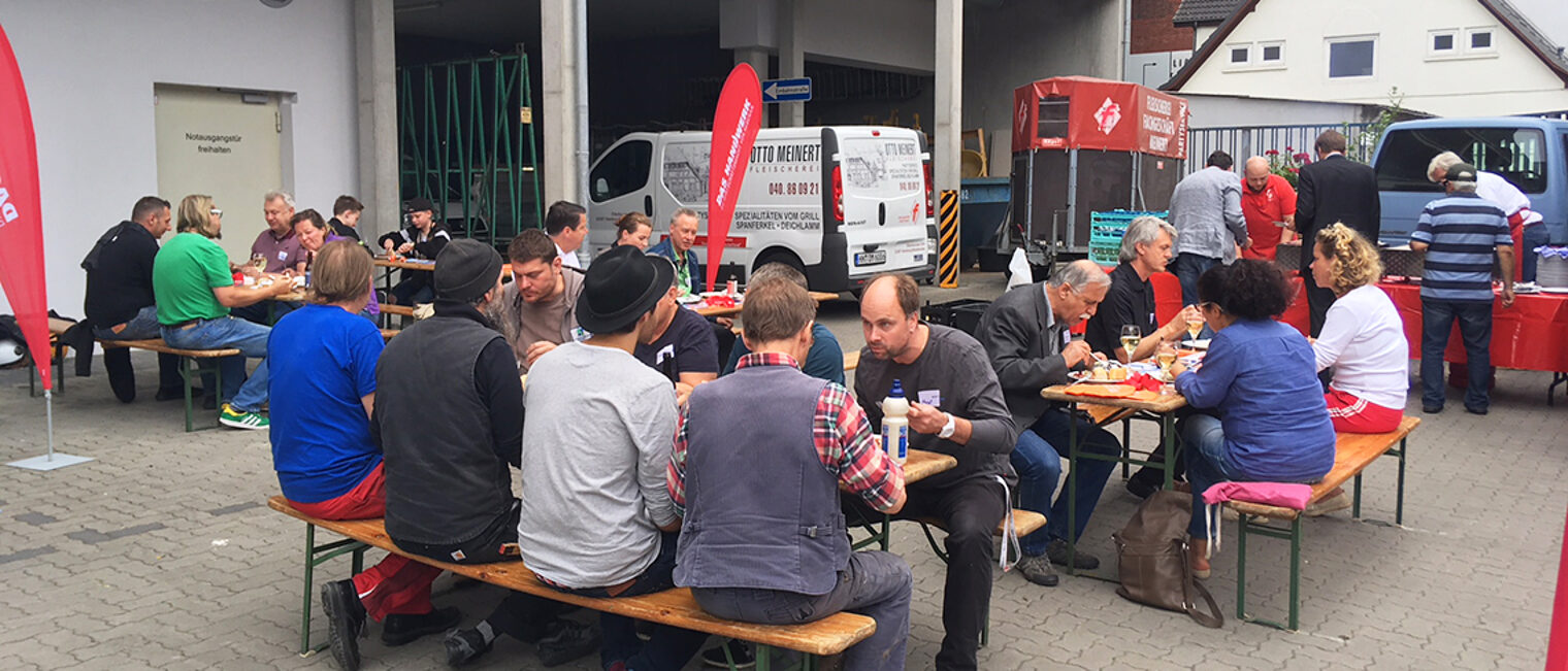 Menschen auf Holzbänken beim Essen.