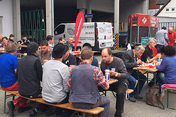 Menschen auf Holzbänken beim Essen.