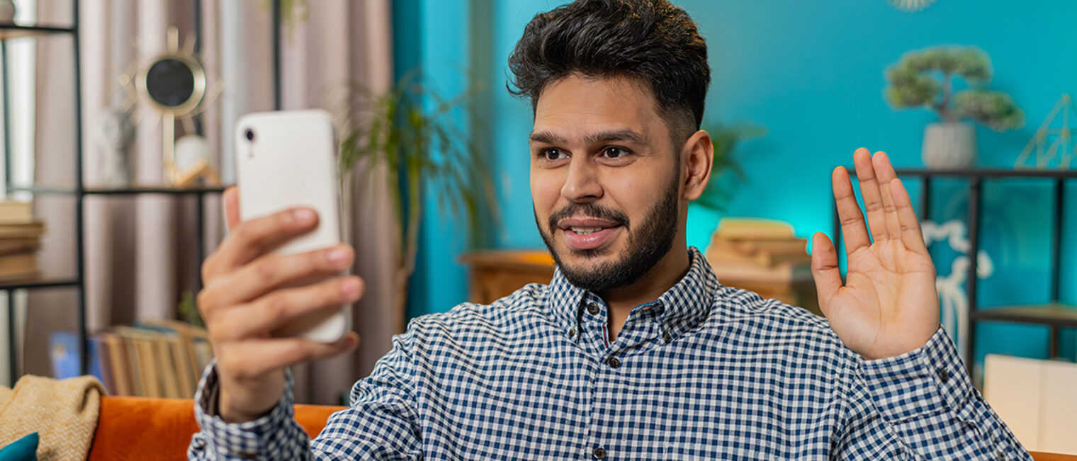 Mann grüßt beim Video-Call mit dem Smartphone.