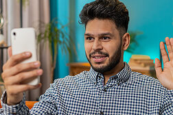 Mann grüßt beim Video-Call mit dem Smartphone.