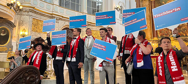 Jungmeisterinnen und -meister halten im Michel Schilder mit Gewerke-Bezeichnung hoch.