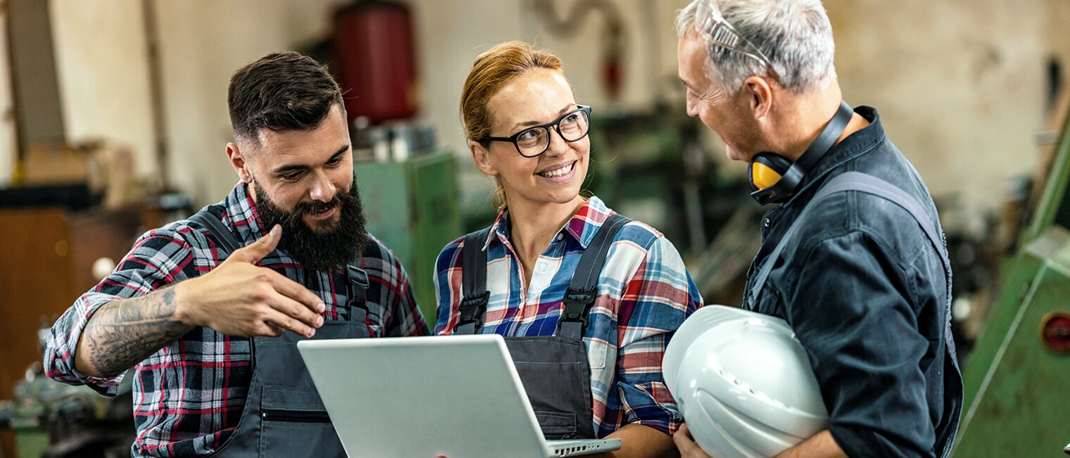 Zwei männliche und und eine weibliche Handwerkerin in einer Werkstatt mit geöffnetem Laptop