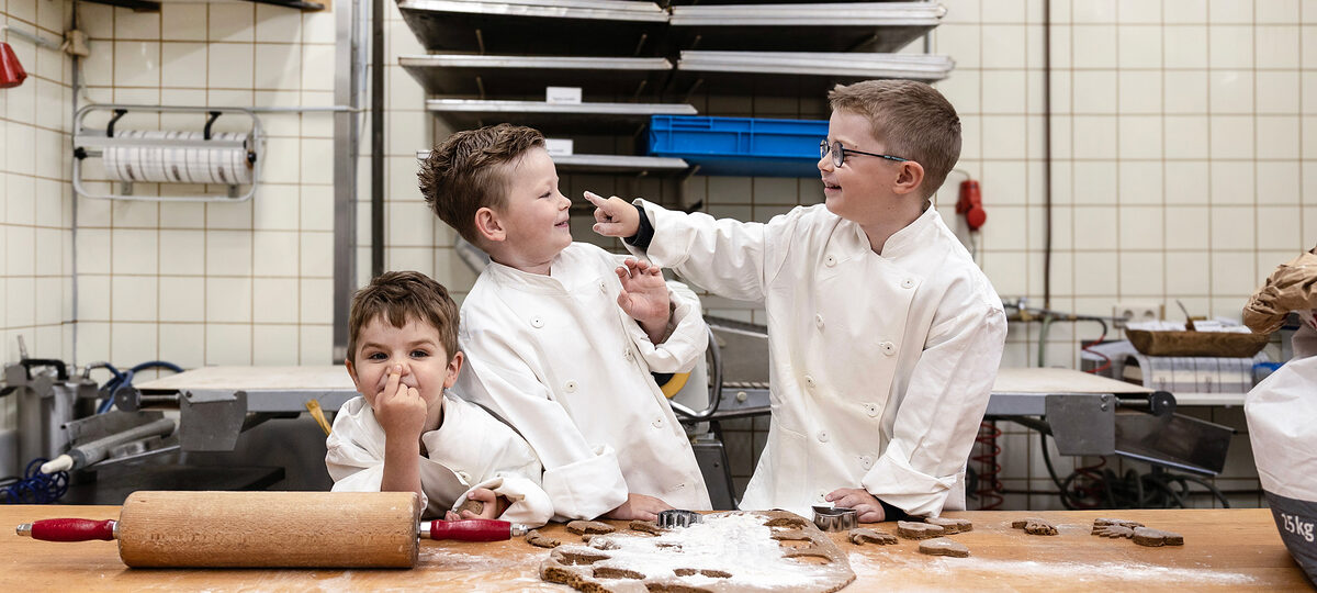 drei Jungen in Bäckerkleidung beim Keksebacken