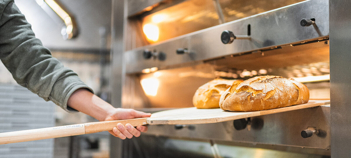 Bäcker holt Brotlaibe aus dem Backofen.