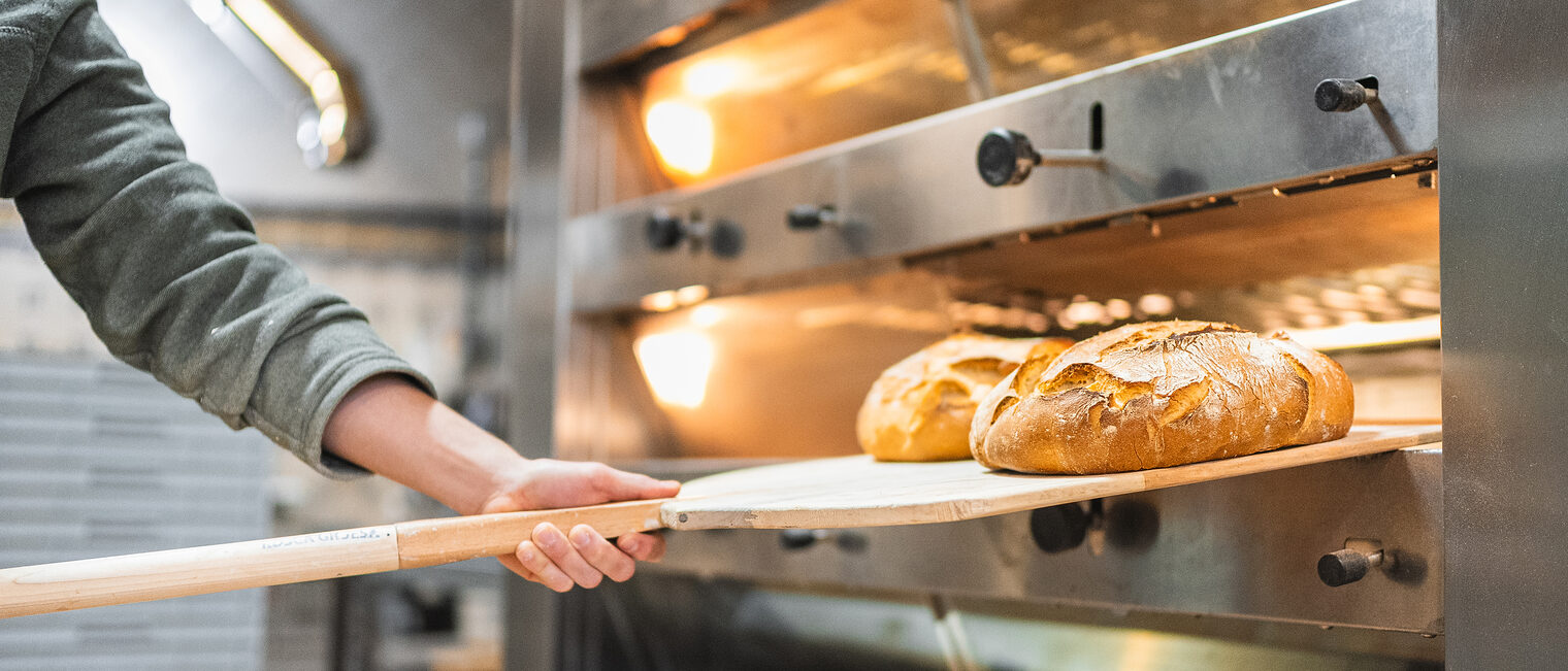 Bäcker holt Brotlaibe aus dem Backofen.