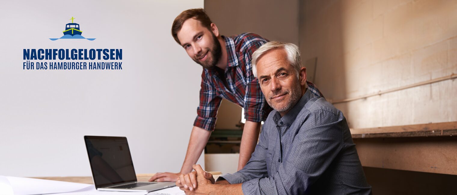 Älterer und jüngerer Mann vor Laptop in einer Werkstatt