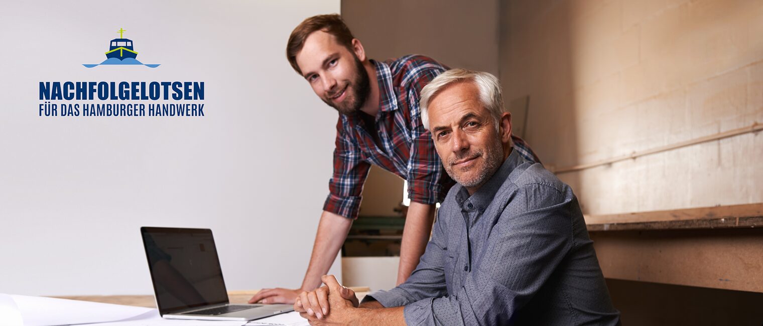 Älterer und jüngerer Mann vor Laptop in einer Werkstatt