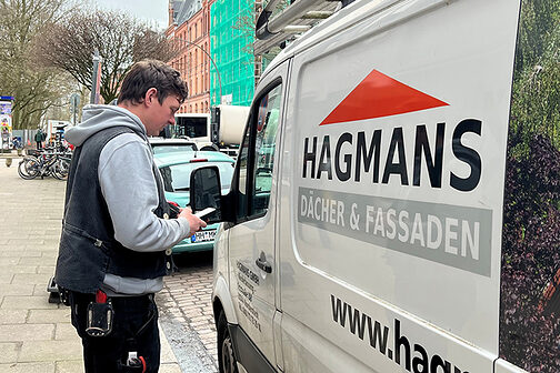 Handwerker steht mit Smartphone neben Transporter