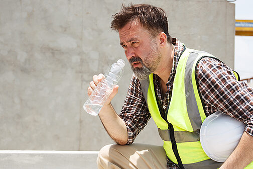 Bauarbeiter trinkt Wasser bei großer Hitze.
