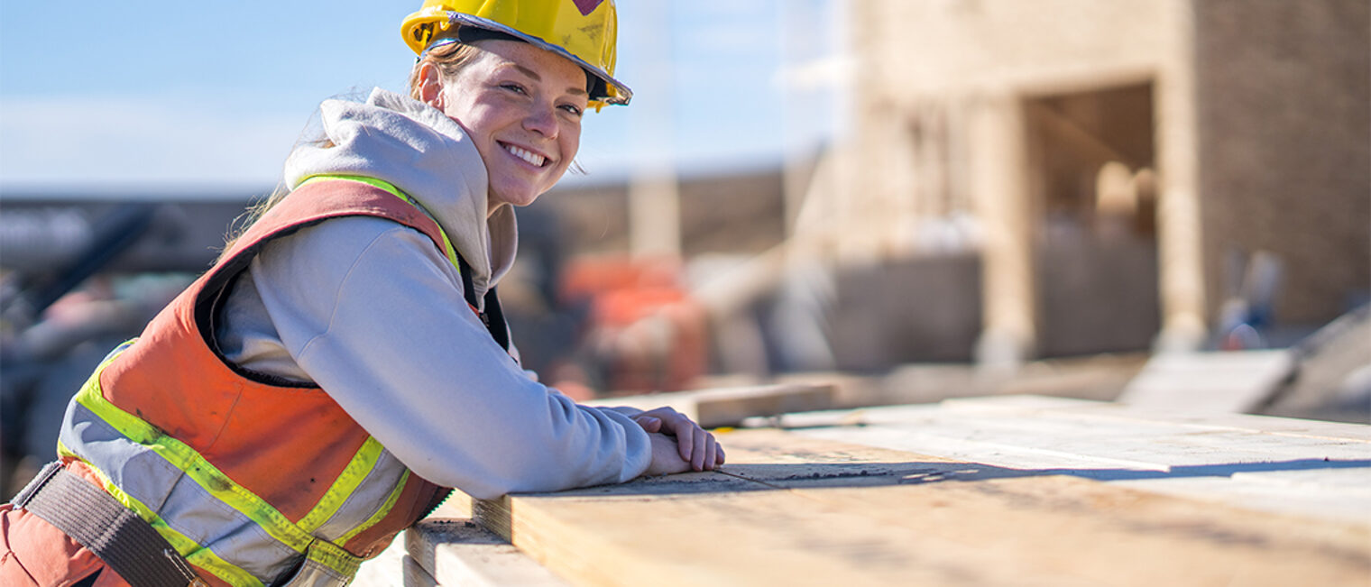 Bauhandwerkerin lehnt auf einem Holzstapel