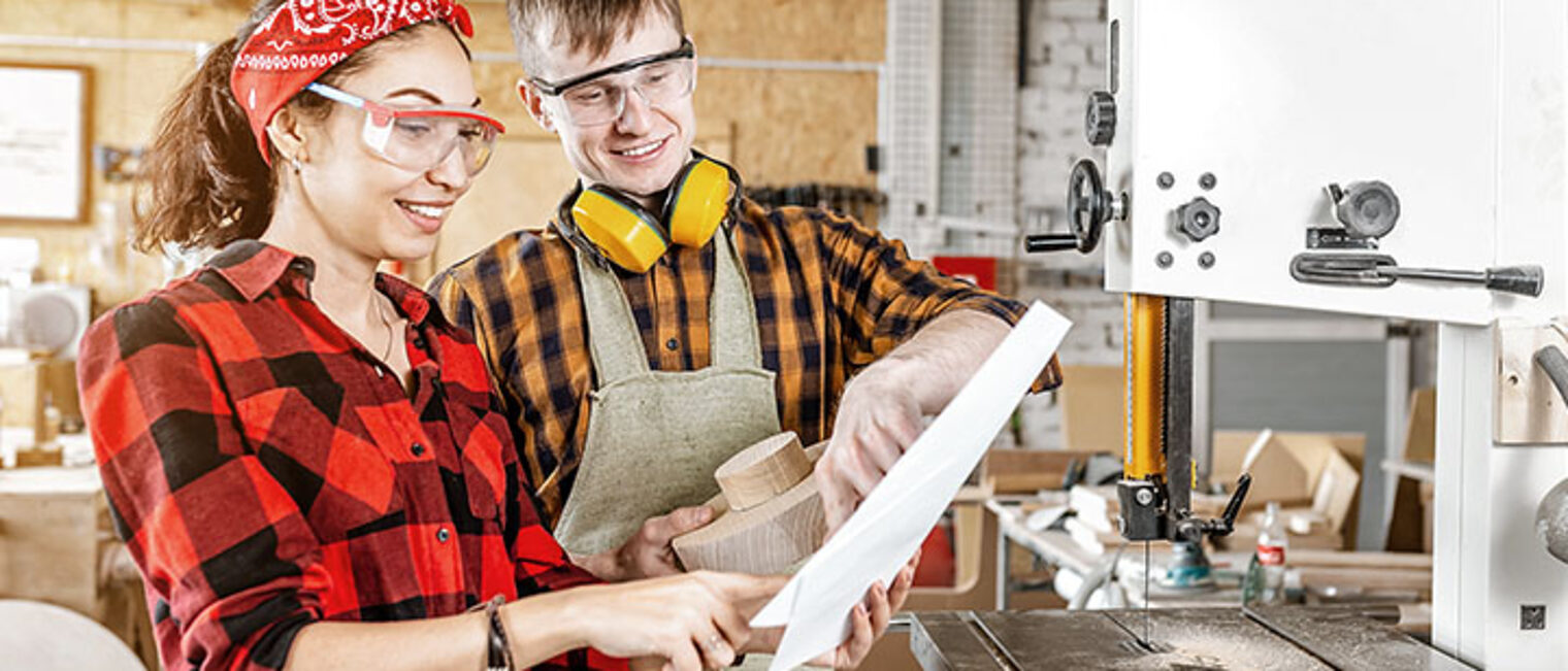 Man and woman colleagues look at the blueprints on the paper in the interior of a modern wood workshop