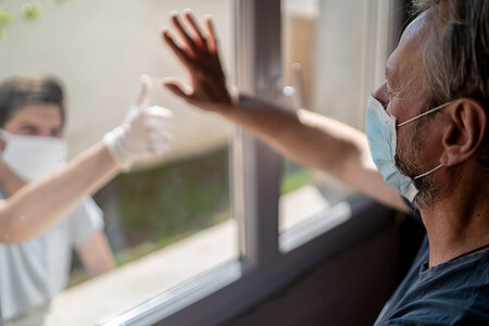 Grandfather and his grandson in protective masks are sadly looking into the window. Image with selective focus and toning Schlagwort(e): protective mask, risk zone